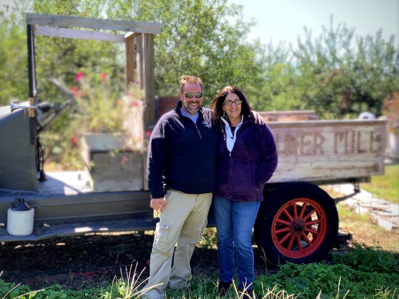 man and woman posing for a picture in front of a small tractor in a field