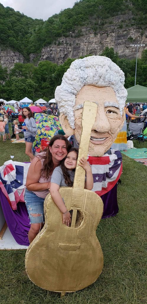 two woman posing for a picture with a large guitar and mascot